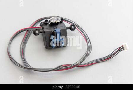 A black electronic sensor with wires and a connector rests on a gray surface Stock Photo