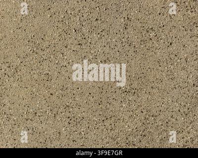 Close-up of a warm beige concrete surface reveals coarse sand, exposed aggregate texture, small pits and irregular marks on an earthy background Stock Photo