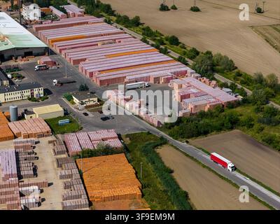 Aerial view of a brick factory storage yard with rows of stacked clay bricks, industrial buildings, and a truck driving on a nearby road in Konin, Wie Stock Photo