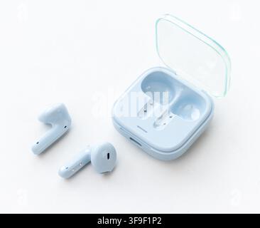 Light blue wireless earbuds and their open charging case rest on white Stock Photo