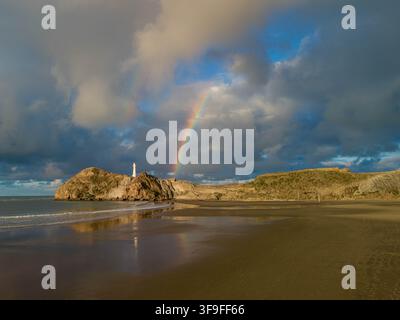 Aerial view of the Castlepoint Lighthouse on a rocky headland above a sandy beach with a rainbow in the dramatic cloudy sky, Castlepoint, Wellington R Stock Photo
