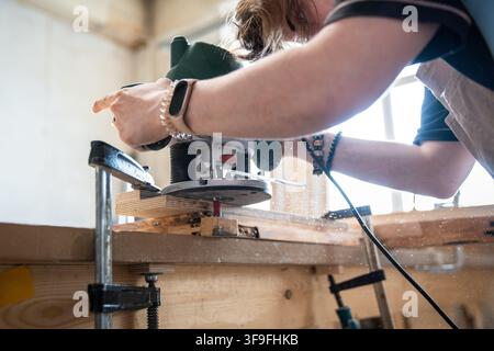 Skilled woman carpenter working with electric wood router machine at workplace in woodworking studio Stock Photo