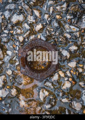 Top view of a single old rusty metal hexagonal nut resting on wet gravel stone ground outdoors Stock Photo