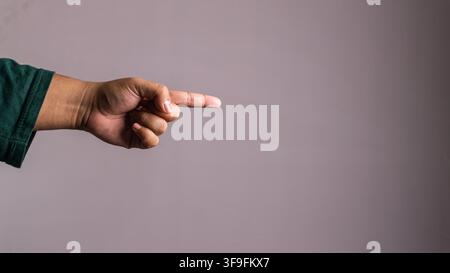 A single human arm points an index finger directly toward the right side against a smooth grey studio background. The unrecognizable Asian male wears Stock Photo