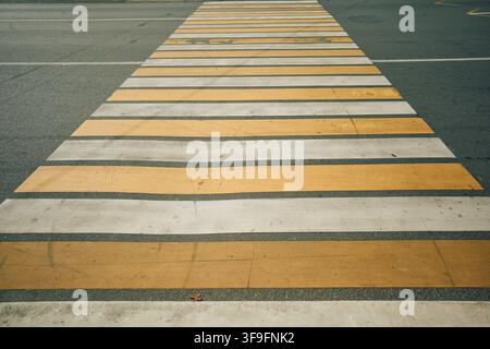 Worn yellow and white pedestrian crossing stripes across asphalt road with top-down view, peeling paint, scuff marks, cracks, urban safety surface Stock Photo