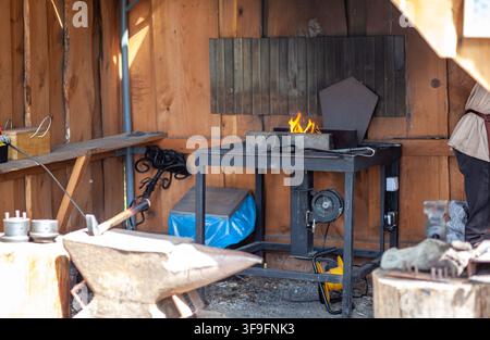 Blacksmith workshop interior featuring an anvil, forge with flames, and various tools on a workbench in a rustic wooden setting Stock Photo