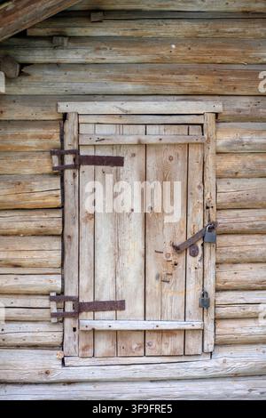 Wooden door with metal latch and padlock on rustic log cabin wall, showcasing natural textures and craftsmanship in a rural setting Stock Photo