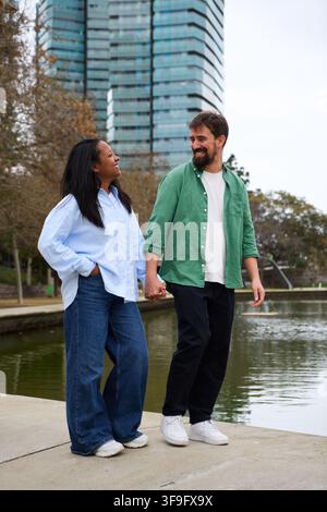Happy multiracial couple holding hands and walking by the river in a city park. Stock Photo