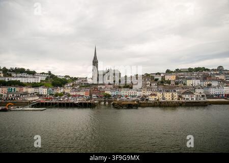 St Colman’s Cathedral rises above the colorful waterfront of Cobh beneath dramatic clouds over Cork Harbour. Stock Photo