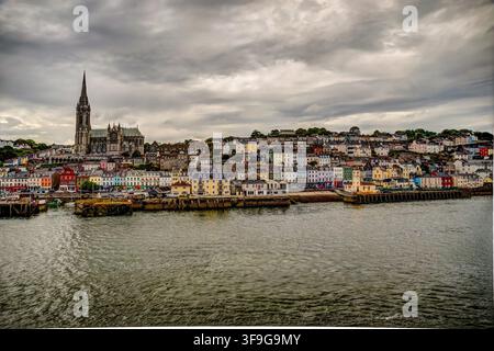St Colman’s Cathedral rises above the colorful waterfront of Cobh beneath dramatic clouds over Cork Harbour. Stock Photo