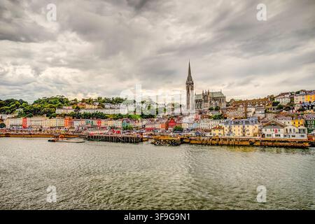 St Colman’s Cathedral rises above the colorful waterfront of Cobh beneath dramatic clouds over Cork Harbour. Stock Photo