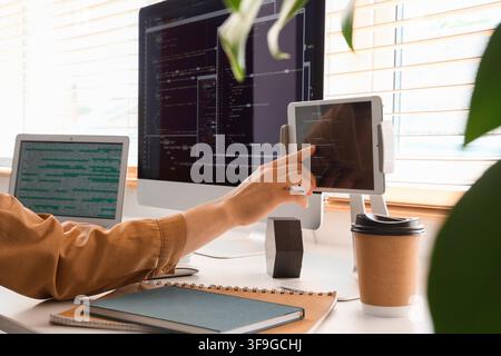 Programmers hand touching a tablet screen with code, multiple monitors displaying software development, modern office workspace Stock Photo