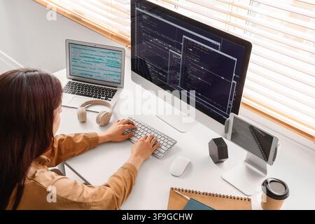 Female programmer coding on multiple screens at a modern home office desk, software development and remote work Stock Photo