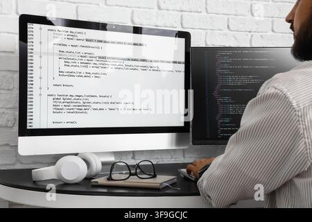 Male programmer coding on computer monitors with headphones and glasses on desk, software development concept, a male programmer is actively coding on Stock Photo
