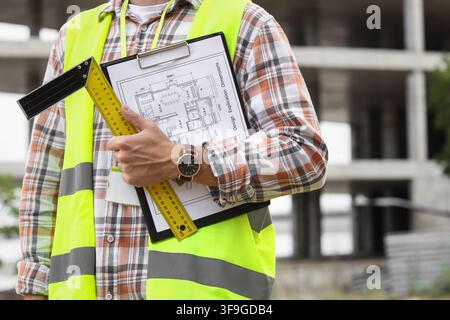 Construction worker in safety vest holding blueprints and ruler at building site, architecture and engineering concept, the image focuses on the profe Stock Photo