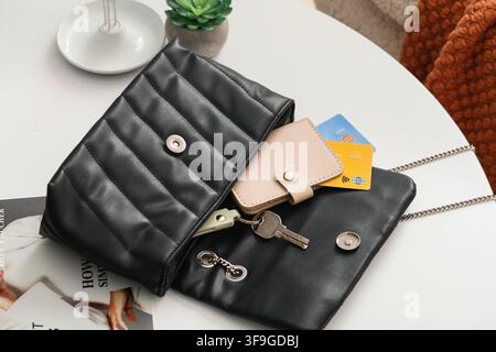 Black quilted leather shoulder bag with wallet, credit cards, and keys on a white table, fashion and personal accessories Stock Photo