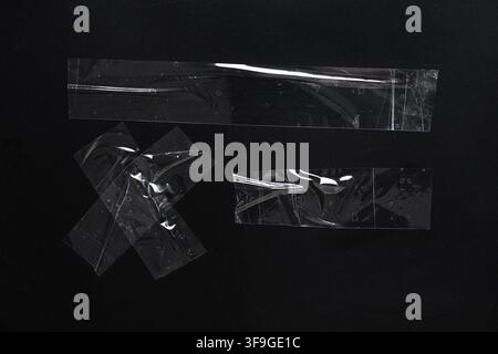 Clear adhesive tape strips and cross shapes on a dark black background, abstract texture and design element Stock Photo