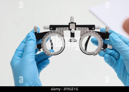 Optometrist hands in blue gloves holding a trial frame for vision testing and eye examination, Precision and care involved in professional eye care an Stock Photo