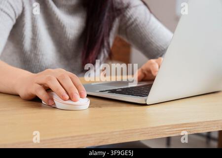 Womans hand using a white computer mouse on a wooden desk with a laptop, remote work and digital communication concept, Modern technology and connecti Stock Photo