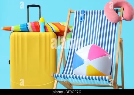 Yellow suitcase with beach umbrella and sunscreen next to a striped deck chair with a beach ball and neck pillow, Yellow suitcase with a colorful beac Stock Photo