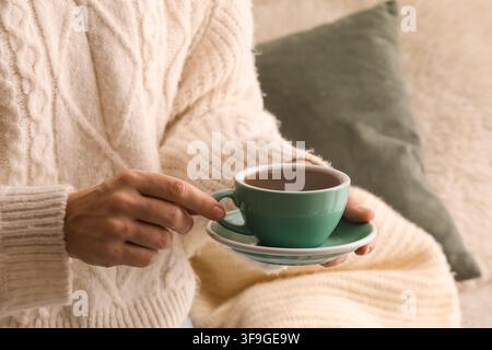 Woman in a cozy cable knit sweater holding a warm cup of tea with a saucer, comfort and relaxation concept, the hot beverage provides a sense of calm Stock Photo