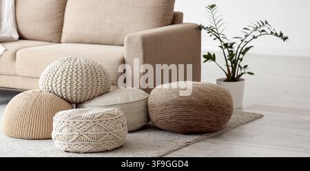 Cozy living room interior with comfortable beige sofa, various knitted poufs, and a green houseplant on a light rug Stock Photo