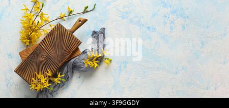 Wooden cutting board with forsythia branches and gray fabric on a light blue textured background Stock Photo