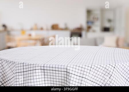 Empty round table with a white and black checkered tablecloth in a blurred modern home interior, the blurred background features a modern home interio Stock Photo