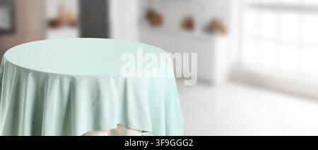 Round table with a light mint green tablecloth in a blurred bright room, empty surface for product display, the empty surface provides ample copy spac Stock Photo