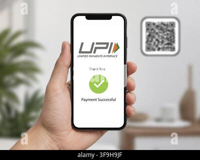 In this photo illustration, A hand holds a smartphone displaying a successful UPI digital payment confirmation, with a QR code visible in the softly b Stock Photo
