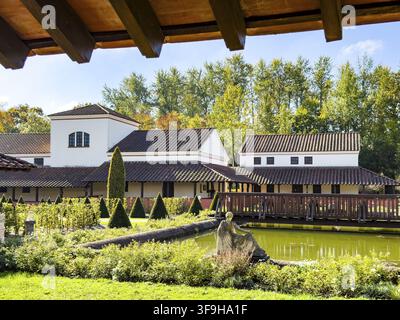 View from site of archaeological open-air museum across small wooden bridge across ornamental pond to reconstructed side wing with restaurant in open- Stock Photo