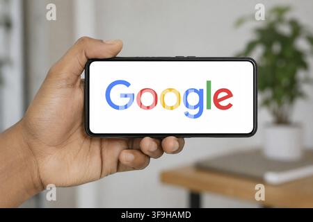 In this photo illustration, a hand holds a smartphone horizontally displaying the Google logo, set against a softly blurred indoor background, in Indi Stock Photo