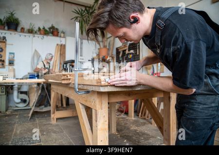Confident handyman in restoration workshop at table working on old wooden window frame renovation. Stock Photo