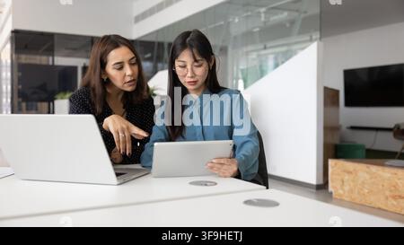 Woman explains data on tablet to young Asian colleague Stock Photo