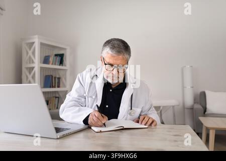 Focused senior man doctor making clinical notes in notebook Stock Photo