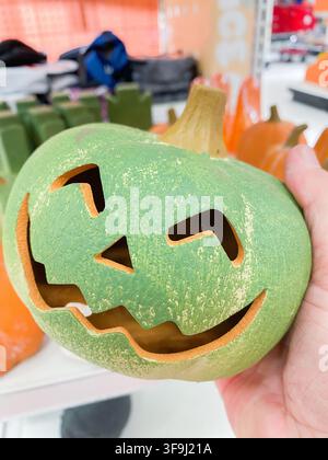 A hand holding a green ceramic jack-o-lantern pumpkin decoration for Halloween - August 8. 2026, Portland Oregon, USA Stock Photo