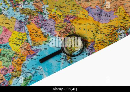A magnifying glass focuses on a world map showing various locations and countries. This scene supports travel planning. Stock Photo