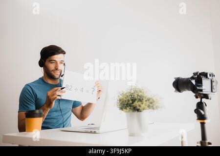 Young man wearing headset talking during online video meeting with laptop and camera Stock Photo