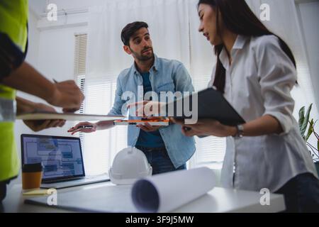 Architects and engineers discussing construction project with blueprint and safety helmet in office Stock Photo