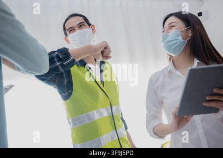 Engineers greeting with elbow bump while wearing face mask during construction meeting Stock Photo