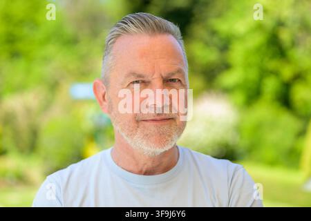 Confident senior man posing outdoors in natural summer light with a calm and serious expression. Authentic lifestyle portrait featuring mature appeara Stock Photo