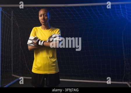 African woman goalkeeper standing in goal on turf, wearing yellow jersey and white gloves Stock Photo