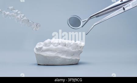 Levitating clear orthodontic aligner, dental mirror, and tweezers above a plaster teeth cast on a blue background. Stock Photo