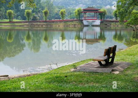 Empty wooden bench overlooking the calm water and red pavilion at Taiping Lake Gardens in Perak, Malaysia. Stock Photo