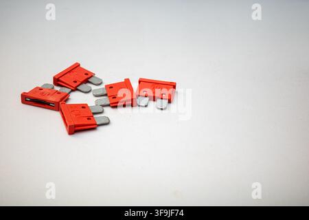 Several red electrical fuses are scattered on a white surface in a workshop. The fuses are used in various electrical applications. The setting sugges Stock Photo