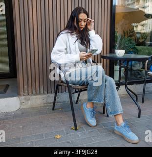 Nice woman sitting in street cafe using smartphone and drinking coffee Stock Photo