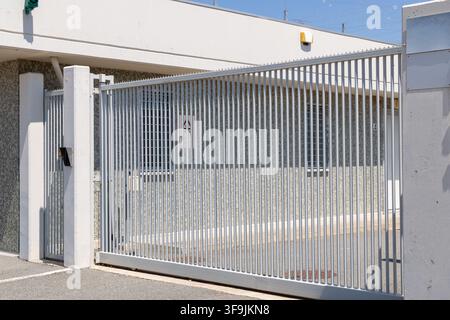 A closed industrial metal gate with vertical bars, featuring an intercom and security camera, suggesting restricted access and surveillance Stock Photo