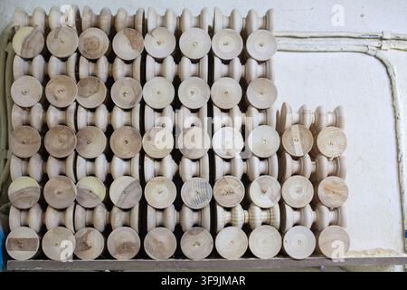 Wooden spools arranged in neat rows on a workbench, showcasing various sizes and textures in a workshop setting Stock Photo