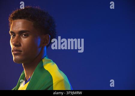 African American man posing, looking left in studio wearing Brazilian flag on shoulders, copy space. Portrait, headshot, closeup, bluebackdrop, green, Stock Photo