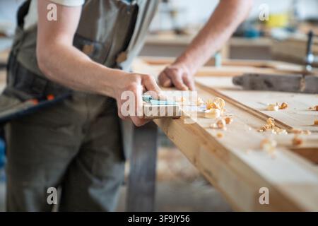 Craftsman holding block with sandpaper and polishing surface of vintage wooden door at worktable Stock Photo